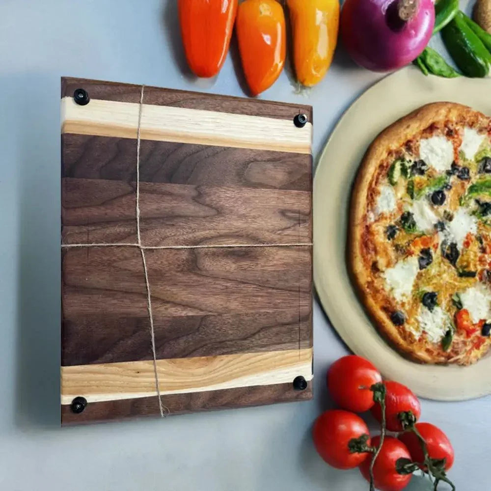 Handcrafted black walnut and hickory cutting board with peg feet, 14x11.5x1 inches, next to fresh vegetables and pizza.
