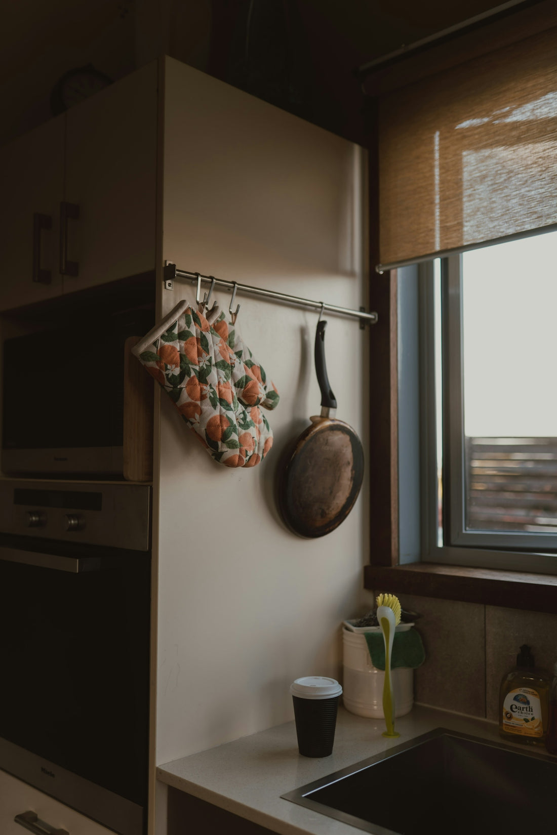 Kitchen counter with hanging pan, oven mitt, and coffee cup.