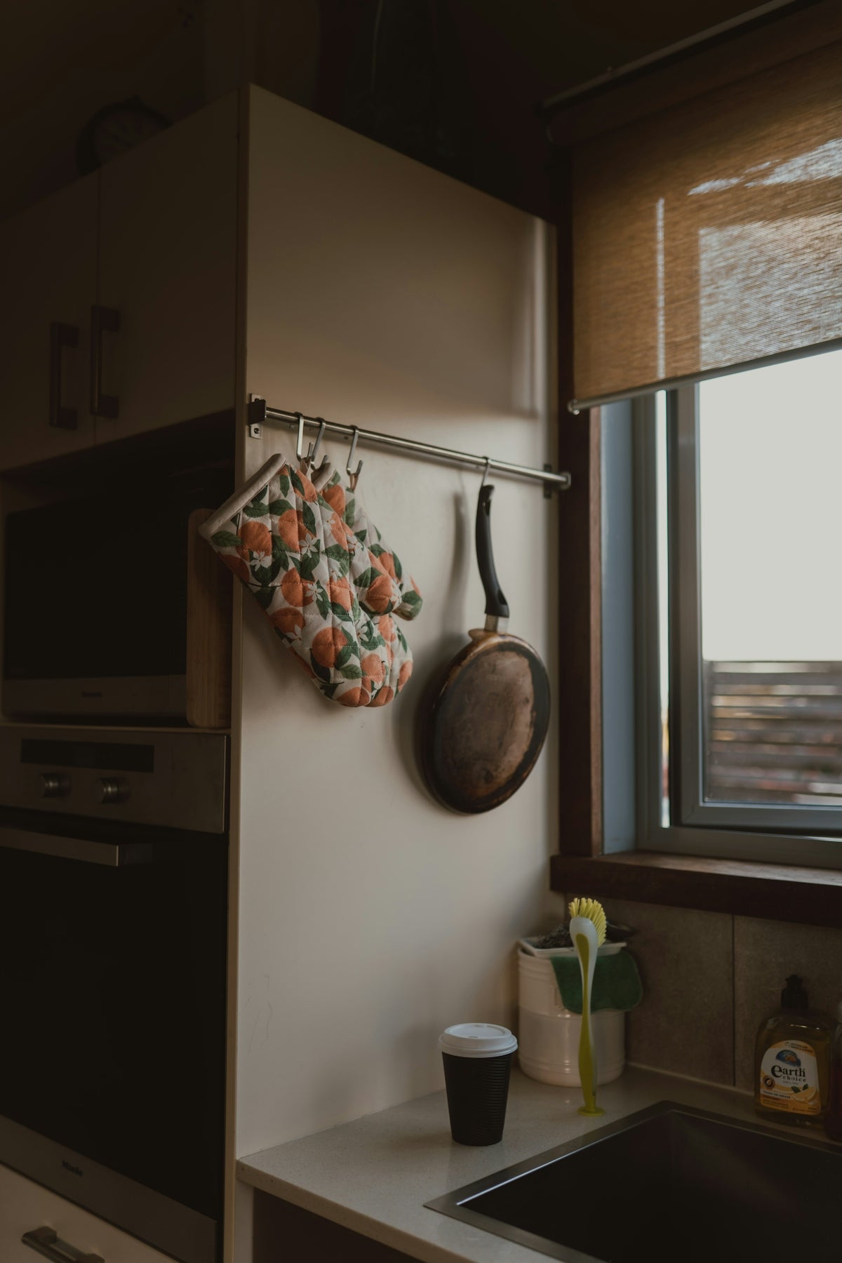 Kitchen counter with hanging pan, oven mitt, and coffee cup.