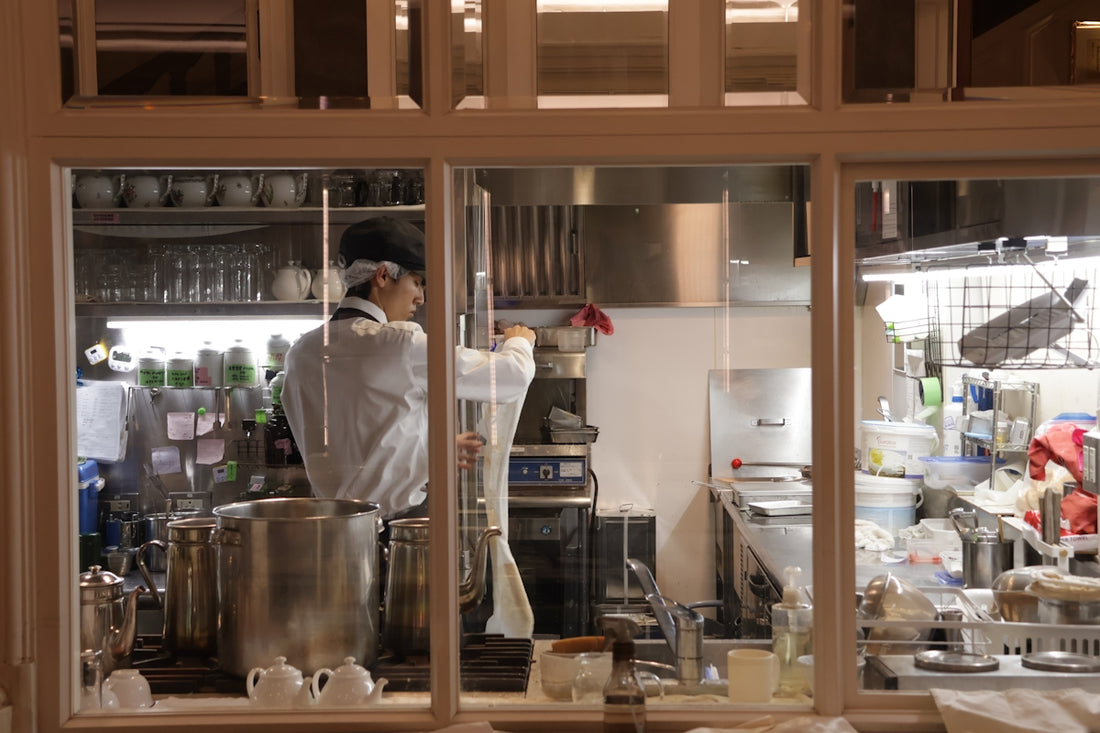 Chef working in a busy professional kitchen through a window.