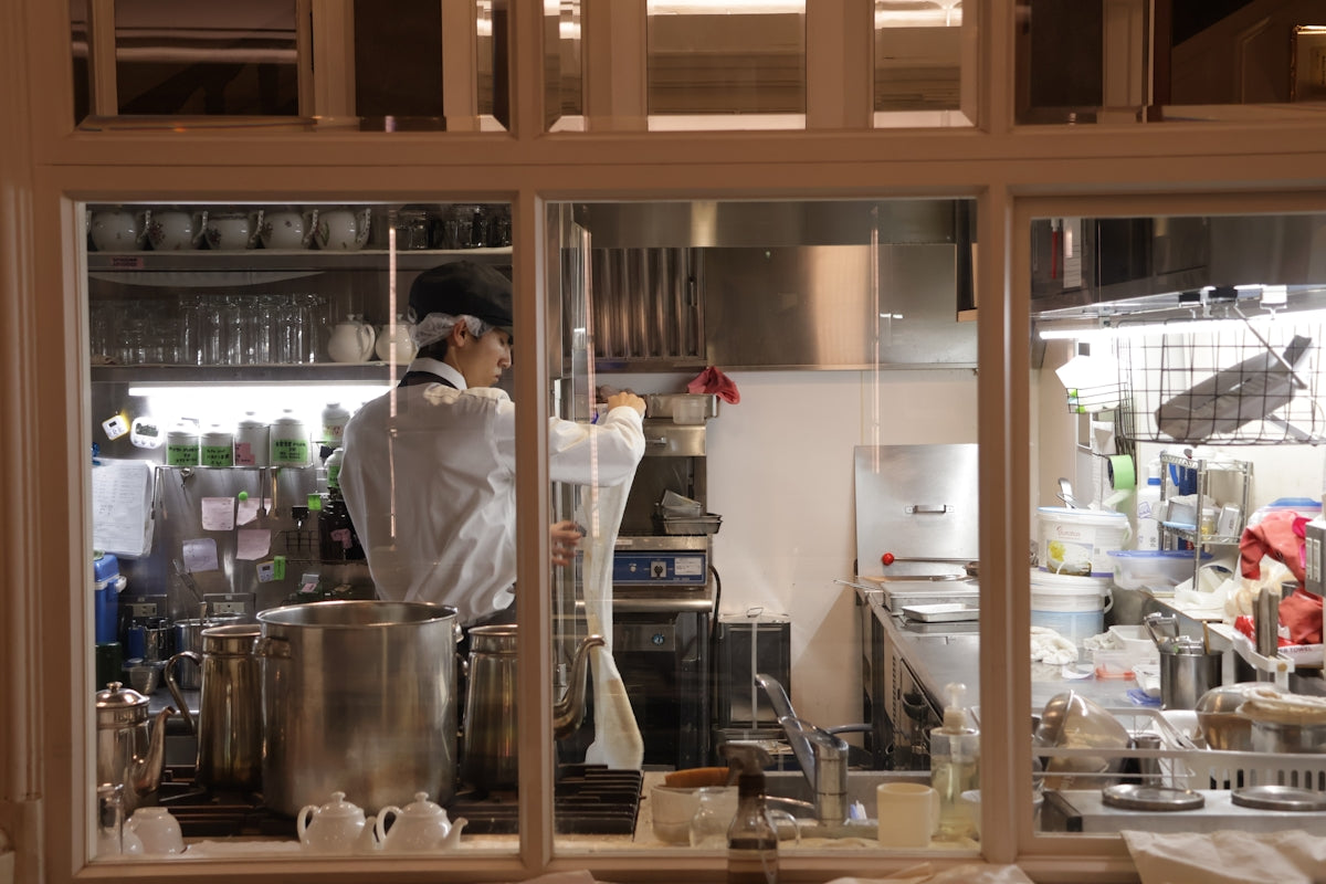 Chef working in a busy professional kitchen through a window.