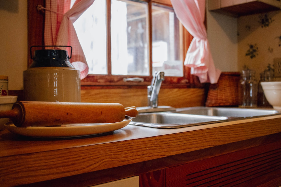 Wooden rolling pin on kitchen counter by sink and window.