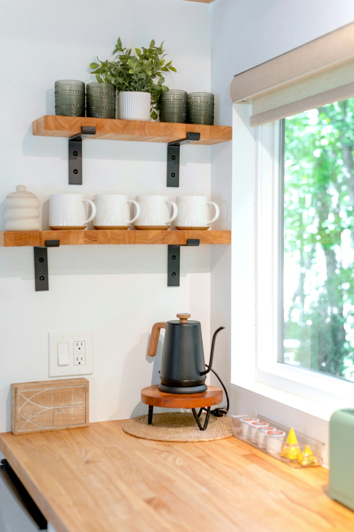 A black electric kettle on a wooden stand in a sunlit kitchen corner
