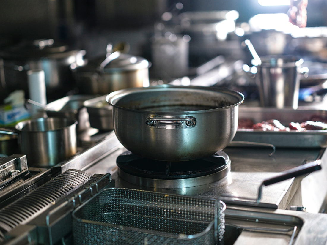Stainless steel pots and a deep fryer basket on a commercial kitchen stove