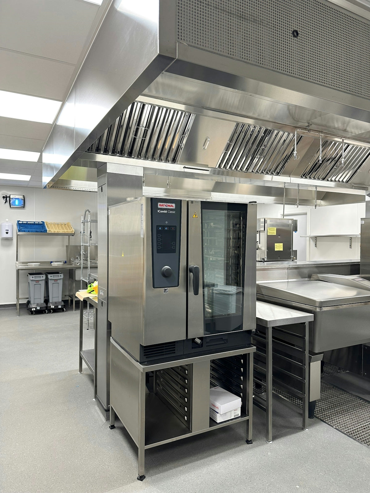 A stainless steel commercial oven in a professional kitchen with a large ventilation hood