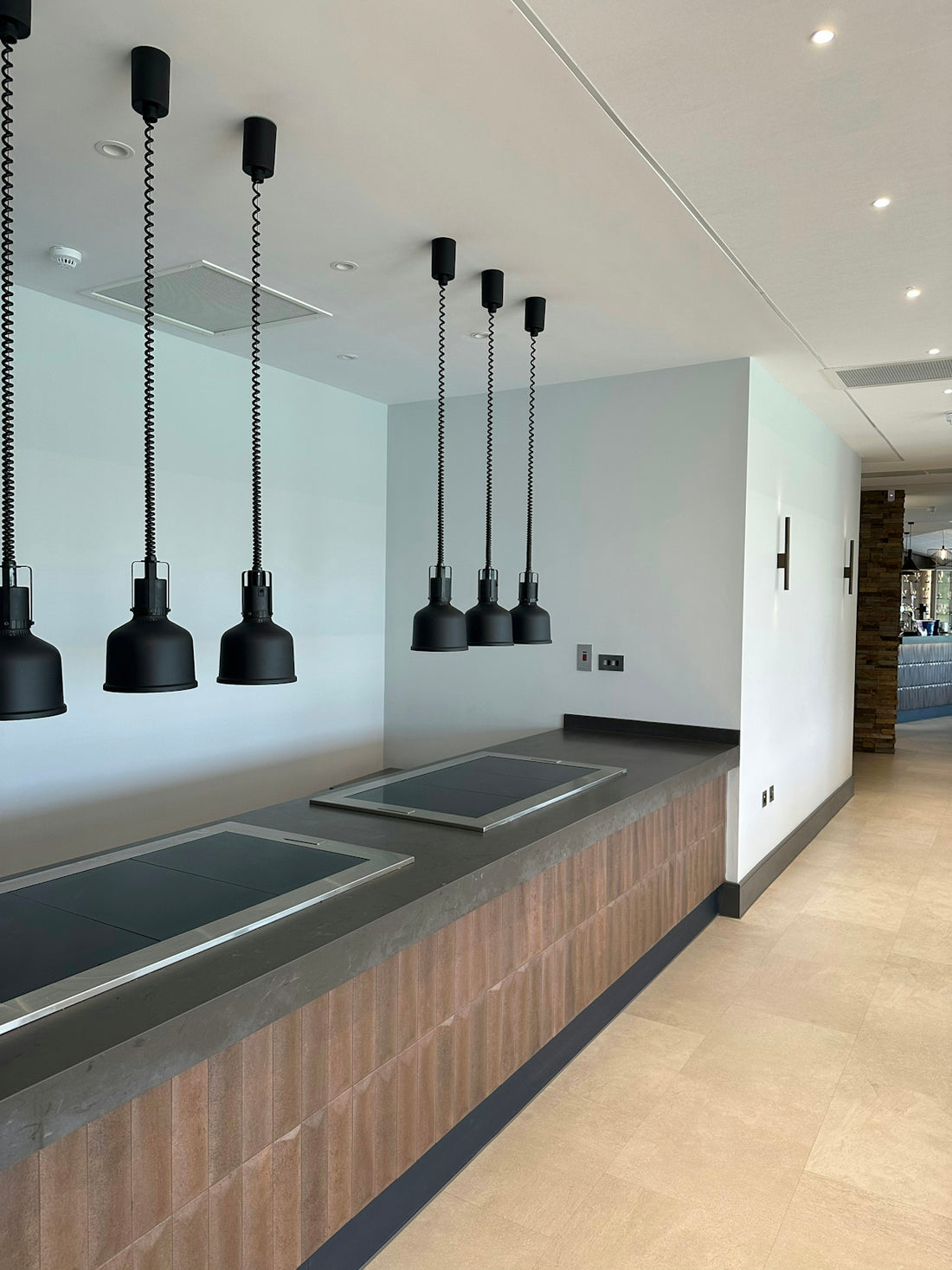 Black pendant lights hanging over a long kitchen counter with integrated induction cooktops