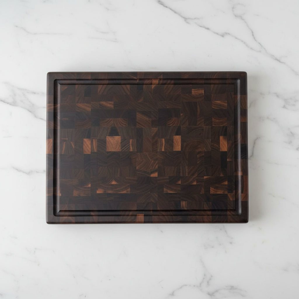 A rectangular wooden cutting board with a dark brown and black geometric mosaic pattern, resting on a speckled granite countertop against a textured wall.