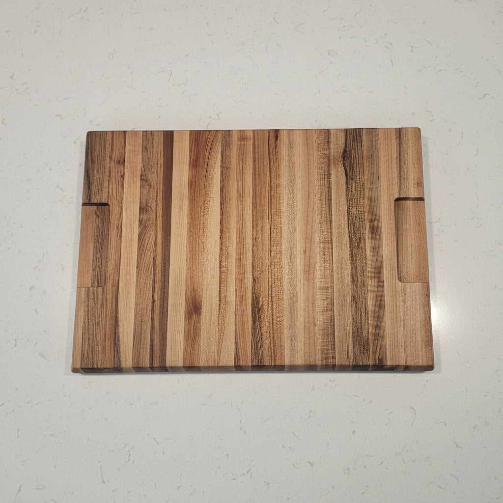 A rectangular wooden cutting board with a natural striped grain pattern, featuring a built-in handle cutout at the bottom and a scoring groove at the top, placed on a speckled granite countertop.