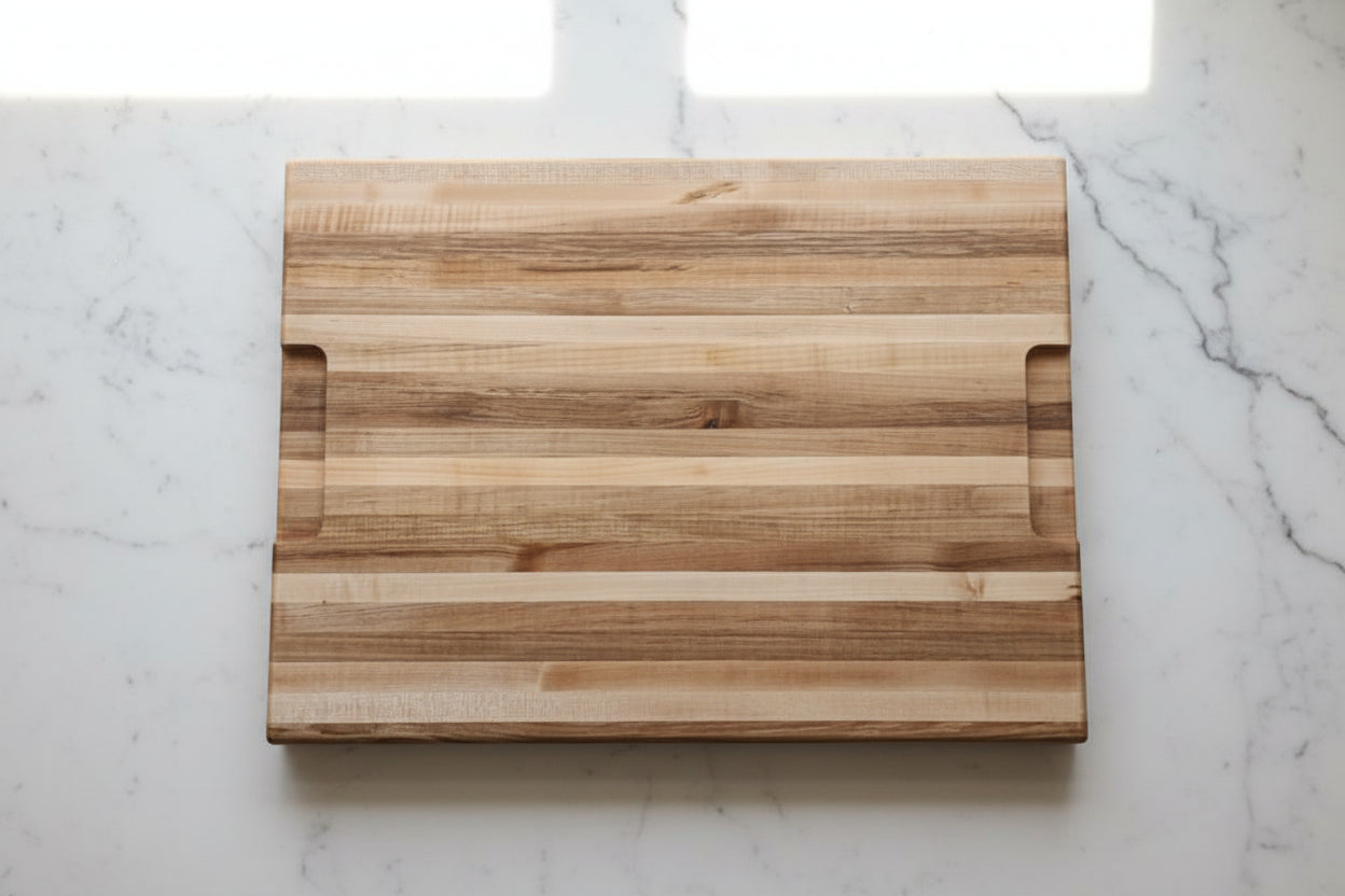 A rectangular wooden cutting board with a striped grain pattern and integrated handle cutouts, resting on a speckled granite countertop.